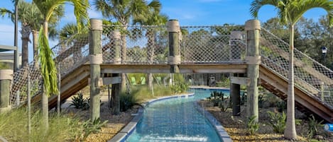 Una piscina con un puente, rodeada de palmeras y un cielo despejado.