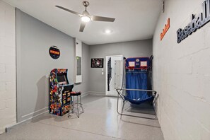 Un couloir avec un ventilateur de plafond, un panier de basket et une borne d’arcade Pac-Man.
