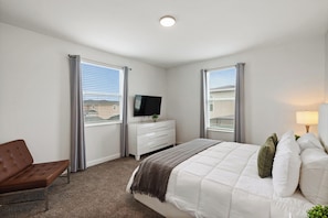 Un dormitorio con una cama, televisión, sillón y cómoda.