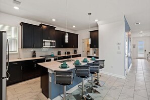 A modern kitchen with dark cabinets, a central island with bar stools, and a stainless steel microwave. - Elegant 5 Bedroom House in Kissimmee, 6701 (Orlando)
