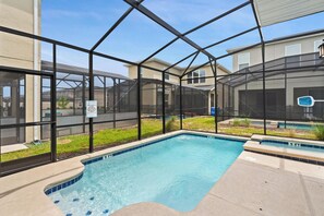 A swimming pool with a glass enclosure, surrounded by a landscaped area with grass and plants. - Elegant 5 Bedroom House in Kissimmee, 6701 (Orlando)