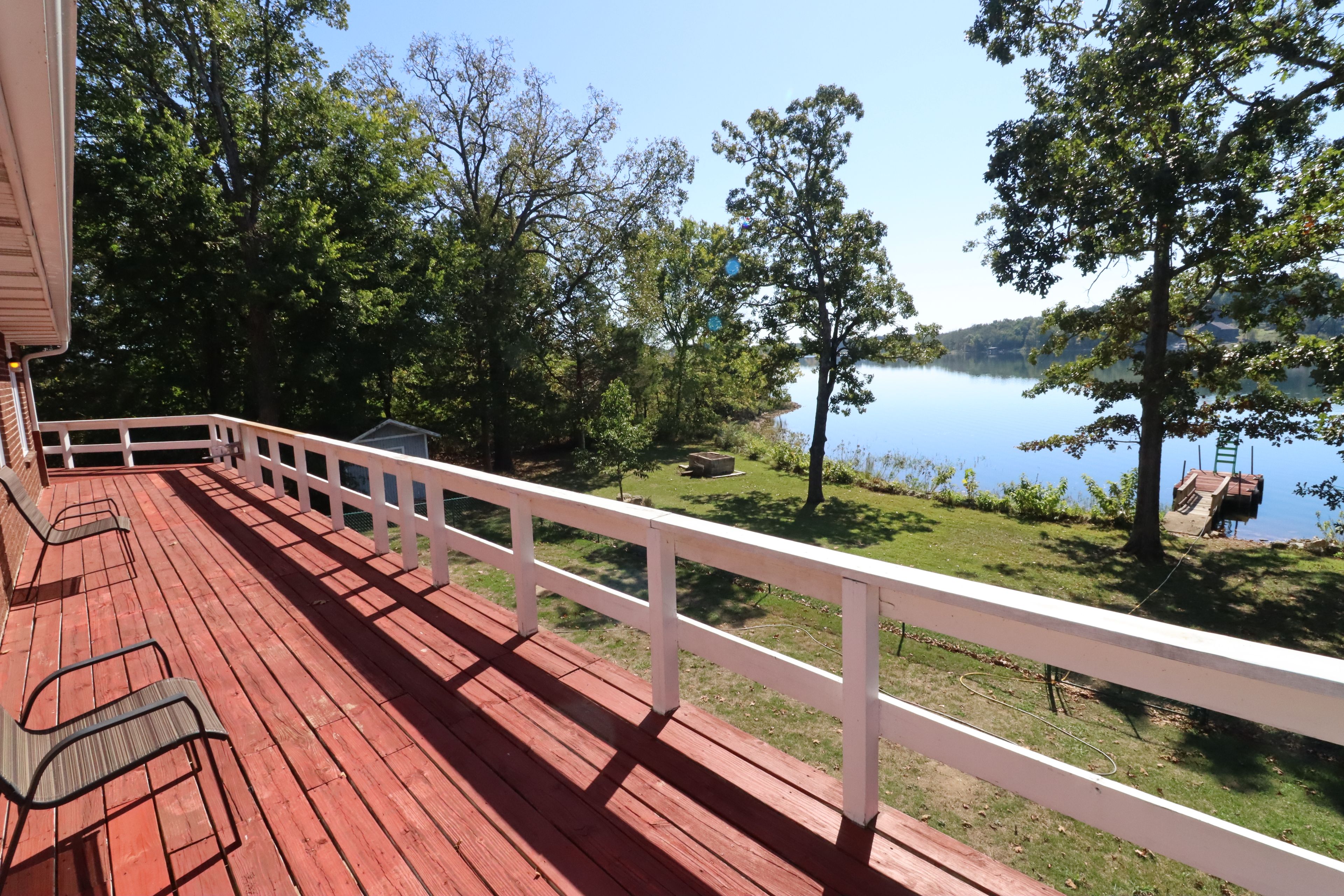 Una terraza de madera con barandilla blanca que da a un lago con árboles y un muelle.