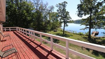 Una terraza de madera con barandilla blanca que da a un lago con árboles y un muelle.