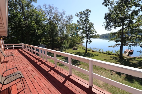 A wooden deck with a white railing overlooking a lake with trees and a dock.