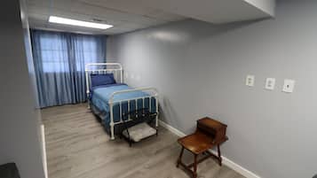 A bedroom with a single bed, a wooden chair, and a window with curtains.
