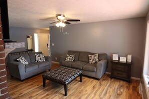 A living room with two sofas, a coffee table, a ceiling fan, and a brick wall.