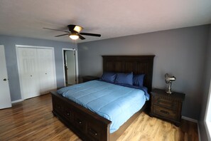 A bedroom with a bed, a nightstand, a ceiling fan, and a door.