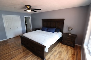 A bedroom with a bed, a nightstand, a ceiling fan, and a door.
