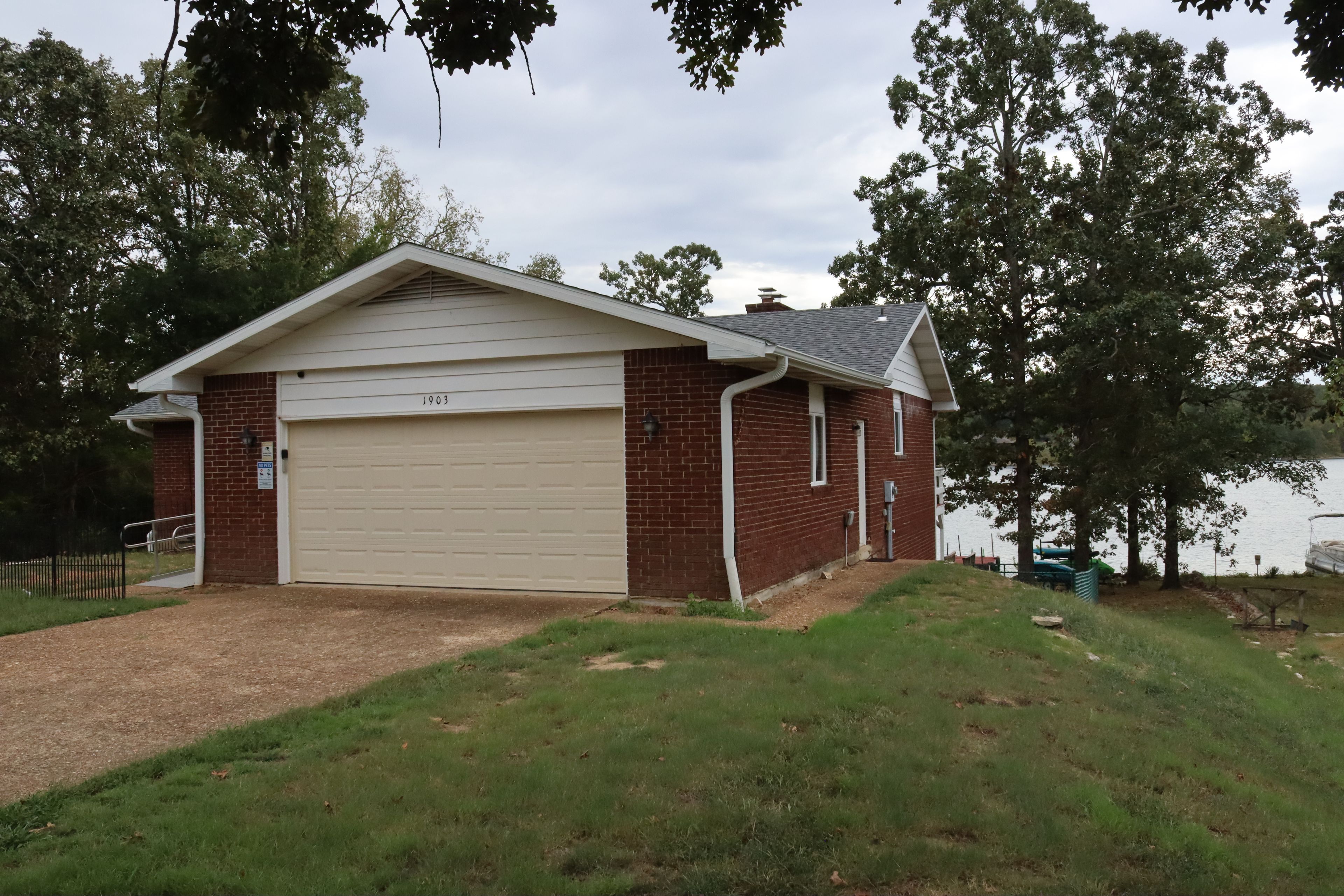 A single-story building with a garage, surrounded by trees and a body of water.