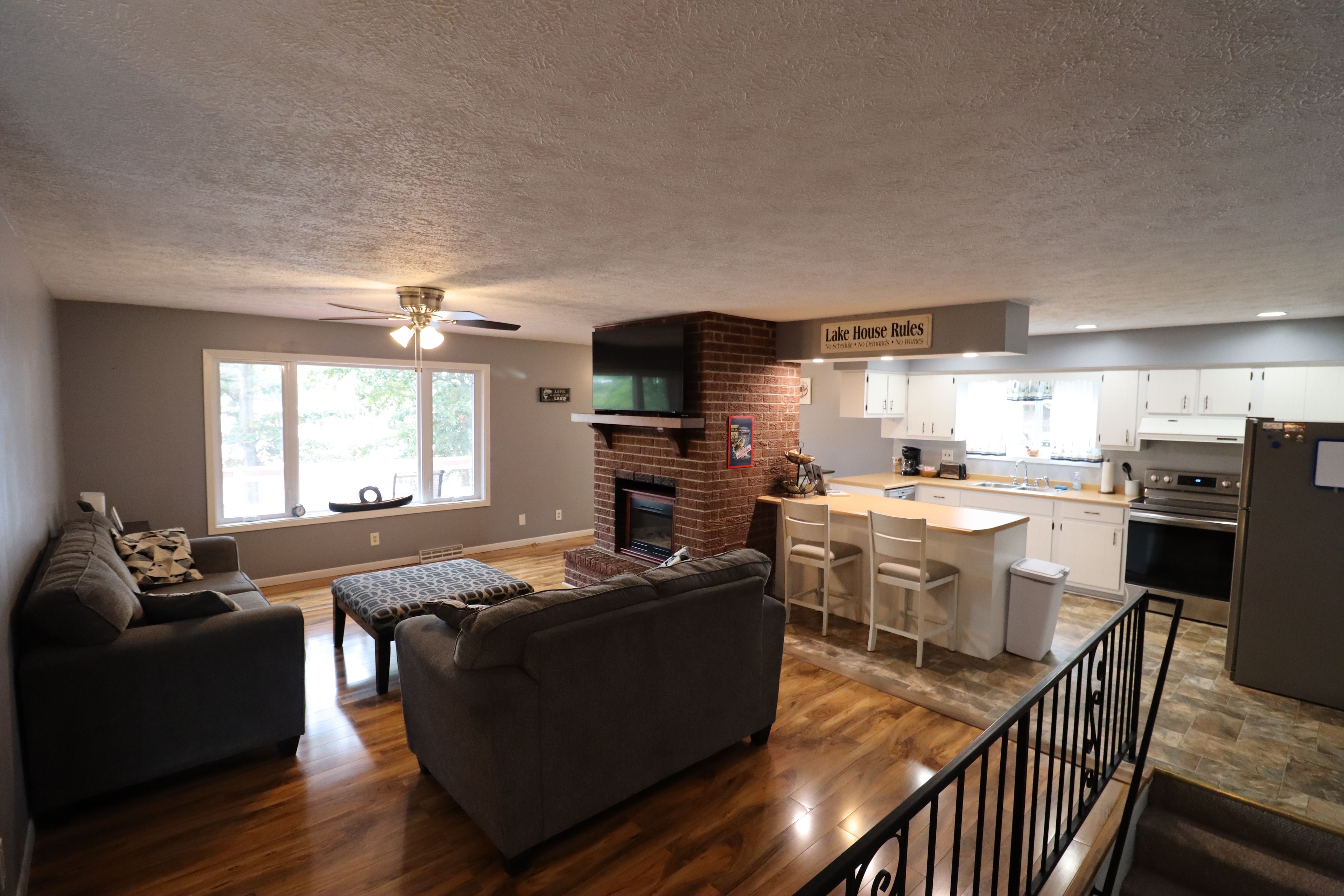 A modern living room with a fireplace, a dining area with bar stools, and a kitchen with white cabinets.