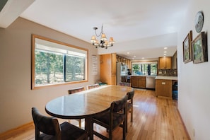 Una cocina moderna con armarios de madera, un comedor con mesa y sillas redondas, y un ventanal con vistas a árboles.