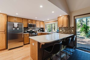 A modern kitchen with wooden cabinets, stainless steel appliances, and a large island with bar stools. - Sunriver Fun - Fireplaces, Hot tub & SHARC (Sunriver)