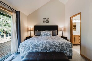 Un dormitorio con una cama grande, dos lámparas de noche, un cabecero con un letrero, un banco de madera y vistas al exterior a través de una ventana.