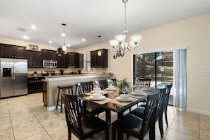 A modern kitchen with dark cabinets, stainless steel appliances, and a dining area with a glass table set for six. - Stunning Family Home in Davenport City, 6698 (Orlando)