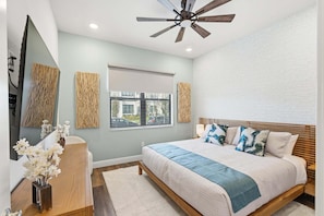 A bedroom with a bed, a ceiling fan, a window with blinds, and a wall-mounted mirror. - Elegant Estate Living in Orlando's Heart, 6697 (Orlando)