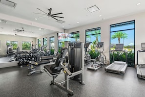 A modern gym with various exercise equipment, large windows, and a ceiling fan. - Elegant Estate Living in Orlando's Heart, 6697 (Orlando)