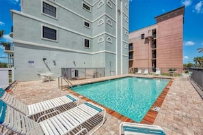 A swimming pool with lounge chairs, a changing room, and a building with multiple windows and balconies. - Secluded 3 Bedroom Condo Sanctuary in Manasota Key, 5942 (Charlotte County)
