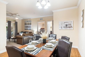 A dining area with a wooden table set for four, surrounded by leather chairs, in a room with beige walls and a ceiling fan. - Serene Retreat: 2 Bed Condo in Davenport, 6707 (Orlando)