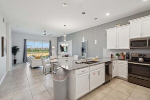 A modern kitchen with white cabinetry, a central island, stainless steel appliances, and a dining area with a view. - Serene Urban Oasis in Davenport City, 6706 (Orlando)