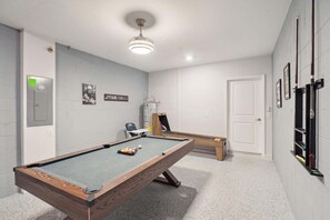 A pool table with a wooden frame and a green felt surface, a ceiling light fixture, and a door with a white frame. - Serene Urban Oasis in Davenport City, 6706 (Orlando)
