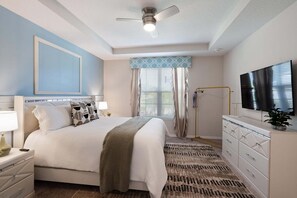 A bedroom with a bed, bedside tables, a TV, a ceiling fan, and a window with blinds. - Luxurious 9 Bedroom Mansion in Kissimmee, 6704 (Orlando)