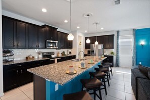 A modern kitchen with dark cabinetry, granite countertops, stainless steel appliances, and pendant lighting. - Luxurious 9 Bedroom Mansion in Kissimmee, 6704 (Orlando)