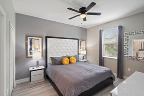 A bedroom with a tufted headboard, two bedside tables with lamps, a bed with a grey quilt, a ceiling fan, and a window with blinds. - Stunning 10 Bedroom Home in Davenport, 6705 (Orlando)