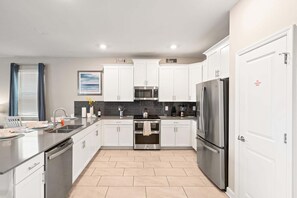A modern kitchen with white cabinets, stainless steel appliances, and a tiled floor. - Stunning 10 Bedroom Home in Davenport, 6705 (Orlando)