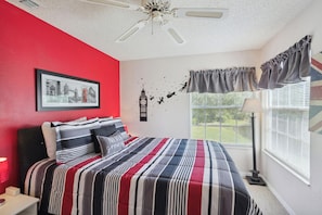 A bedroom with a bed, a ceiling fan, a window with curtains, a wall clock, and a framed picture. - Inviting 3 BR Condo in Kissimmee City, 6703 (Orlando)