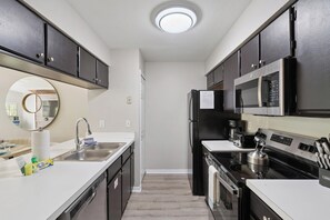 A modern kitchen with dark cabinets, a stainless steel refrigerator, a microwave, a stove, and a sink. - Charming Condo in Kissimmee, 6702 (Orlando)