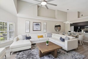A modern living room with a sectional sofa, a coffee table, and a ceiling fan. - Charming Condo in Kissimmee, 6702 (Orlando)