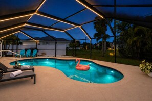 A swimming pool with a flamingo float, lounge chairs, and a covered area with geometric lighting. - Inviting 3 Bedroom Home in Punta Gorda, 5947 (Charlotte County)