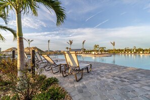 Ein Poolbereich mit Liegestühlen, Palmen und blauem Himmel.