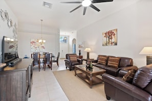 A spacious living room with a brown leather sofa, a dining area with a large table and chairs, and a ceiling fan. - Spacious Family Home in Kissimmee, 6691 (Orlando)
