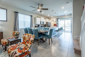A modern kitchen with white cabinets, a central island, and a dining area with blue chairs and a patterned sofa. - Inviting Family Home in Davenport Area, 6695 (Orlando)