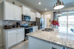 A modern kitchen with white cabinetry, stainless steel appliances, a granite countertop, and a large window providing natural light. - Inviting Family Home in Davenport Area, 6695 (Orlando)