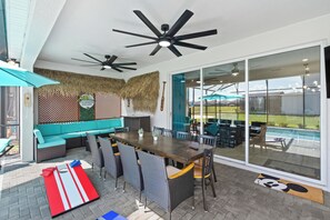 An outdoor dining area with a long table and chairs, a thatched wall, and a view of a swimming pool. - Grand Mansion in Davenport City, 6696 (Orlando)