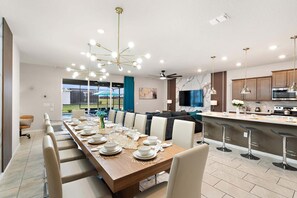 A modern kitchen with a central island, bar stools, and a dining area with a long table set for six. - Grand Mansion in Davenport City, 6696 (Orlando)