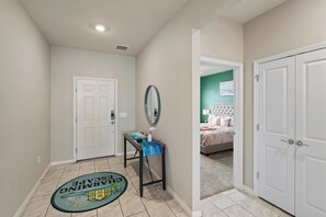 Un couloir avec un paillasson, une porte, un miroir et une chambre à coucher visible à travers une porte ouverte.