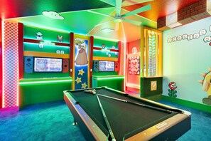Un espace piscine intérieur, bien éclairé, avec une table de billard, des néons et des jeux d’arcade.
