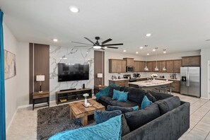 A modern living room with a large flat-screen TV, a dark grey sofa with blue cushions, a wooden coffee table, and a ceiling fan. - Grand Mansion in Davenport City, 6696 (Orlando)