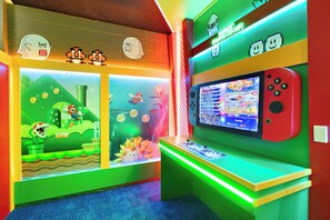 A brightly lit gaming center with a large screen displaying a game, a Nintendo Switch console, and colorful wall decorations. - Grand Mansion in Davenport City, 6696 (Orlando)