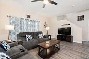 A living room with a sofa, coffee table, TV, and a staircase. - Elegant 4 Bedroom Townhome in Davenport, 6694 (Orlando)