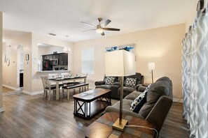 Ein modernes Wohnzimmer mit Essbereich, Deckenventilator und einer Küche im Hintergrund.