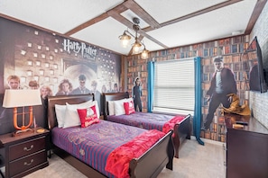 Ein Zimmer mit einem großen Harry Potter Poster, einem Bett mit einer rot- und blau gemusterten Tagesdecke, einem Nachttisch mit einer Lampe und einem Bücherregal voller Bücher.