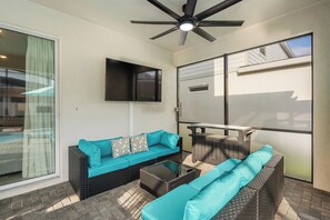 Eine Terrasse mit Deckenventilator, einem an der Wand montierten Flachbildfernseher und einer Sitzecke aus zwei Korbschaukeln mit türkisfarbenen Kissen.