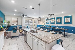 A modern kitchen with a granite countertop, white cabinetry, and a dining area with blue chairs and a table. - Elegant 10 Bedroom Home in Davenport, 6693 (Orlando)