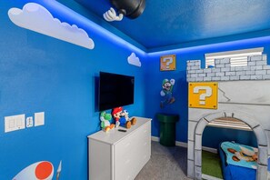 A room with a blue wall, a white dresser, a television, and a Mario-themed play area. - Stunning 8 Bedroom House in Davenport City, 6692 (Orlando)