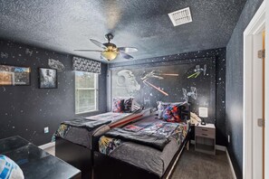 Ein Schlafzimmer mit einem Bett, einem Deckenventilator, einem Fenster mit Jalousien und Wandbildern zum Thema Star Wars.