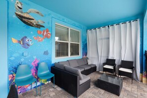 A room with a blue wall mural, a sofa, two chairs, a coffee table, and a window with blinds. - Stunning 8 Bedroom House in Davenport City, 6692 (Orlando)